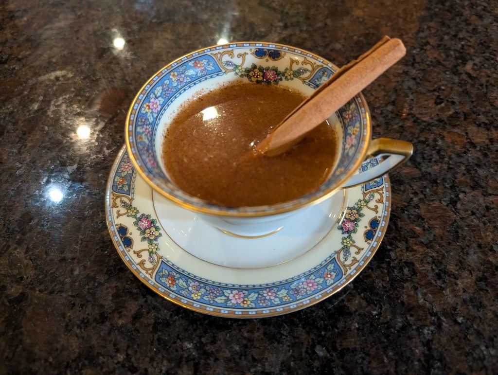 Cider Punch in a china teacup and saucer with a cinnamon stick as a drink stir