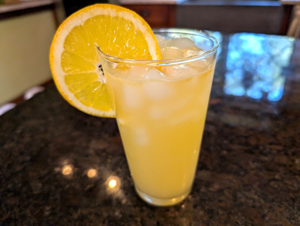 Pineapple citrus mocktail in a highball glass with an absurdly large orange slice as garnish