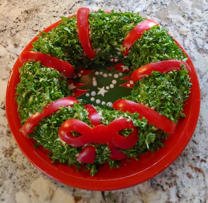 Cheese log shaped into a wreath and covered in parsley and red bell pepper to resemble a holiday wreath
