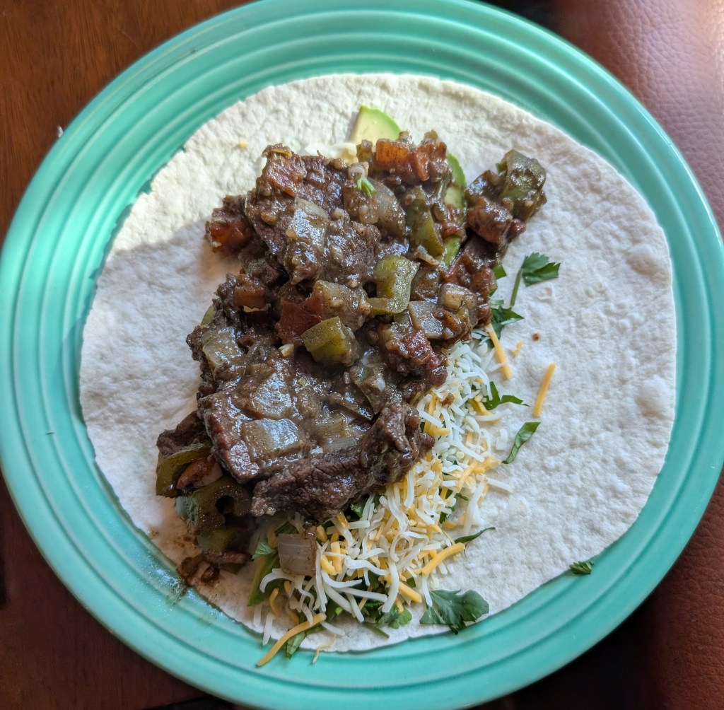 Cochinita pibil served with cheese, avocado, and cilantro on a flour tortilla