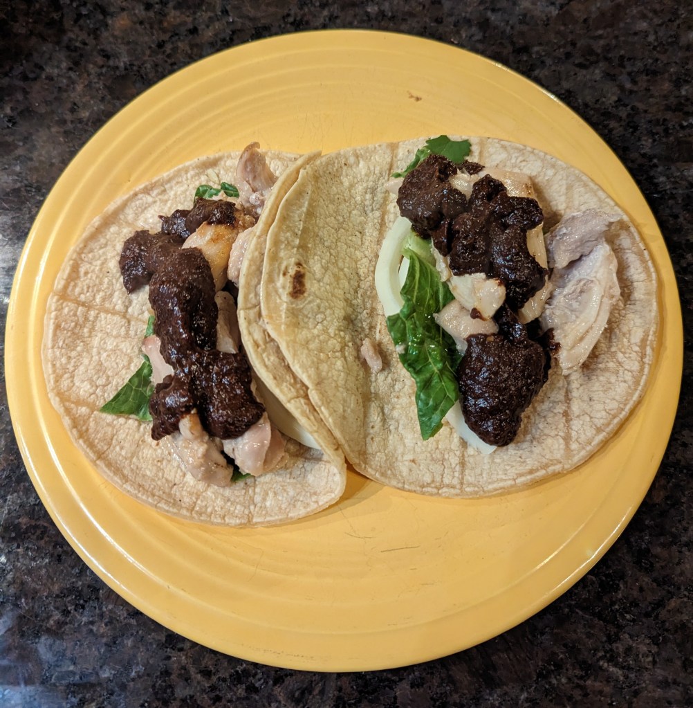 Mole negro added to a taco with turkey, lettuce, and onions on a soft corn tortilla