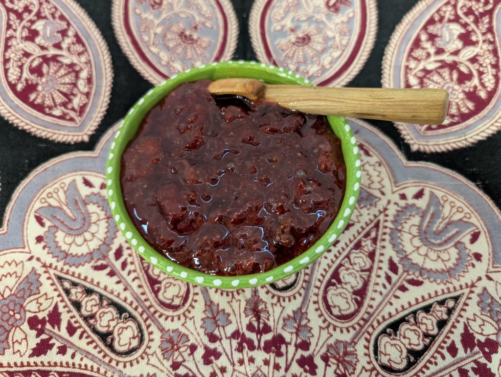 A pint's worth of strawberry jam served in a ceramic bowl with a wooden spoon