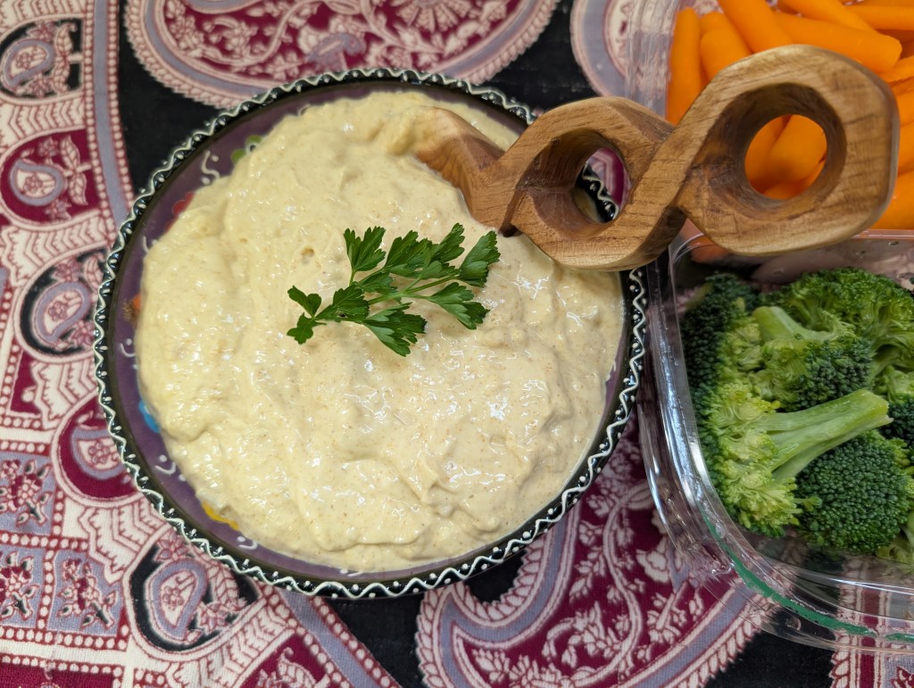 A bowl of curry dip with a wooden spoon and a sprig of parsley. This is the double batch.