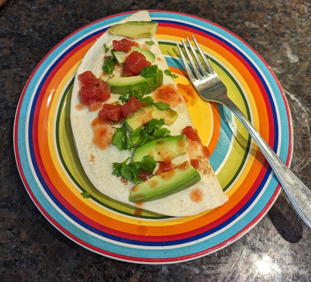 Quesadilla on the plate, dressed with sliced avocado, cilantro, and salsa