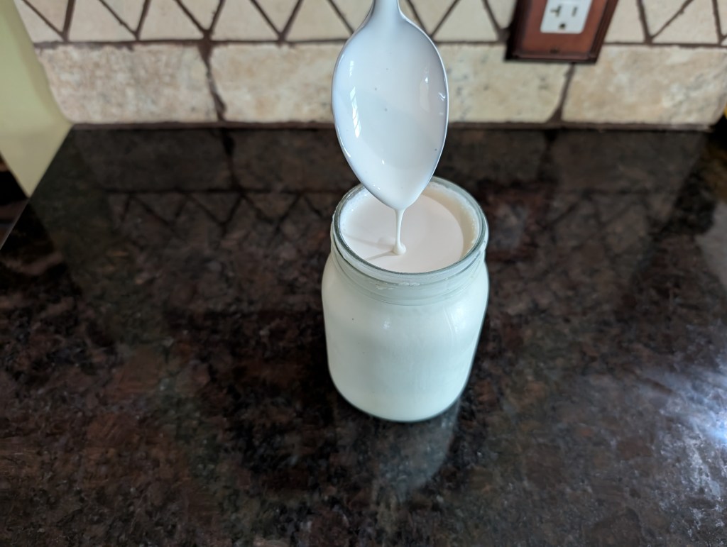 Smetana dripping from a spoon into a very full glass jar