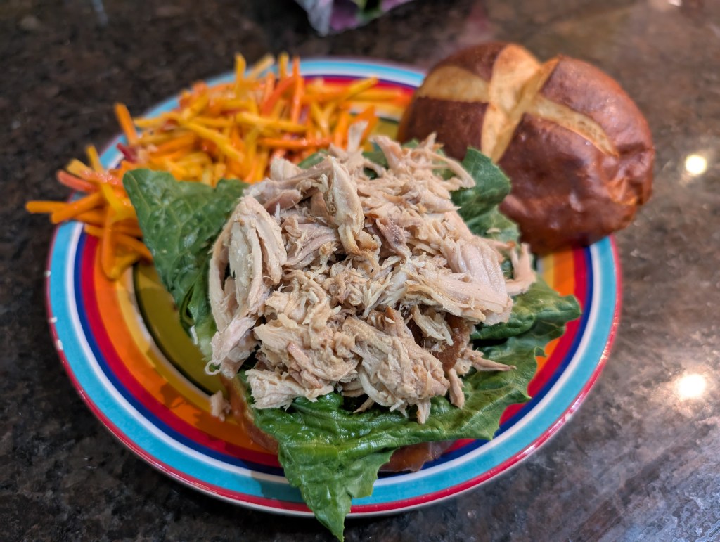 Pulled pork, unseasoned, on a romaine leaf with a pretzel bun and spicy carrot slaw 