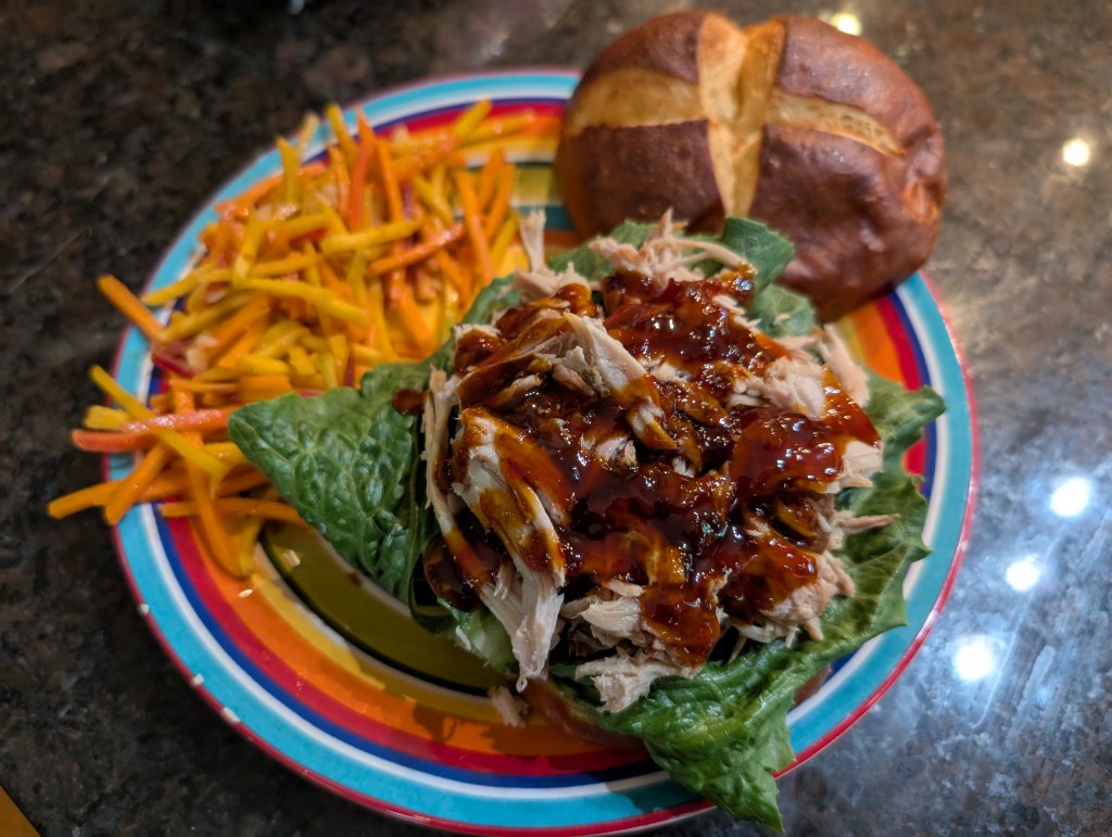 Pulled pork, with sweet chili sauce, on a romaine leaf with a pretzel bun and spicy carrot slaw 