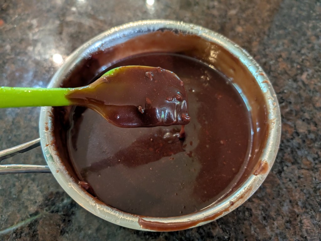 Chocolate Drizzle Icing in the saucepan with a spatula to show a 1/8-inch thick drip while it's still warm