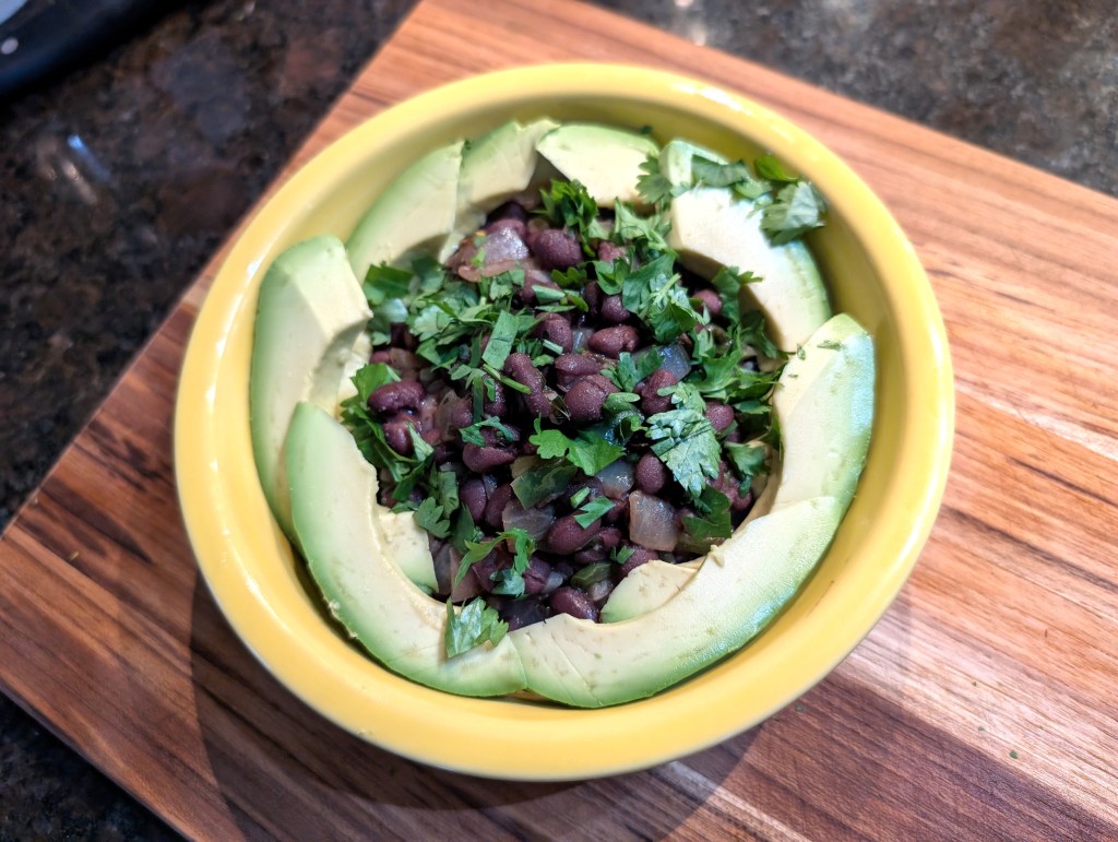 Black beans and rice in a bowl, garnished with avocado slices and cilantro