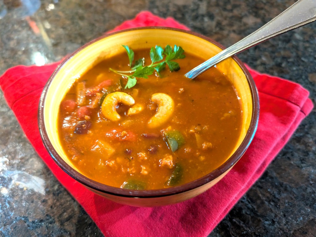 cashew chili in a ceramic bowl with spoon and a sprig of parsley as garnish