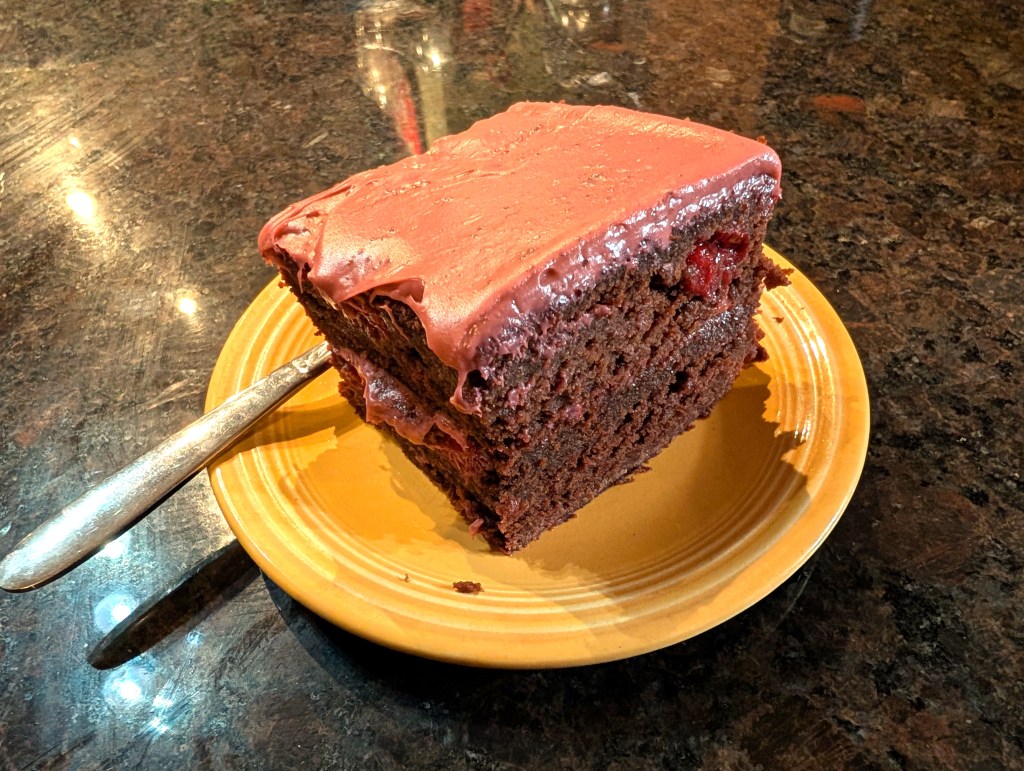 A square slice of chocolate cherry cake, two layers, with cream cheese frosting