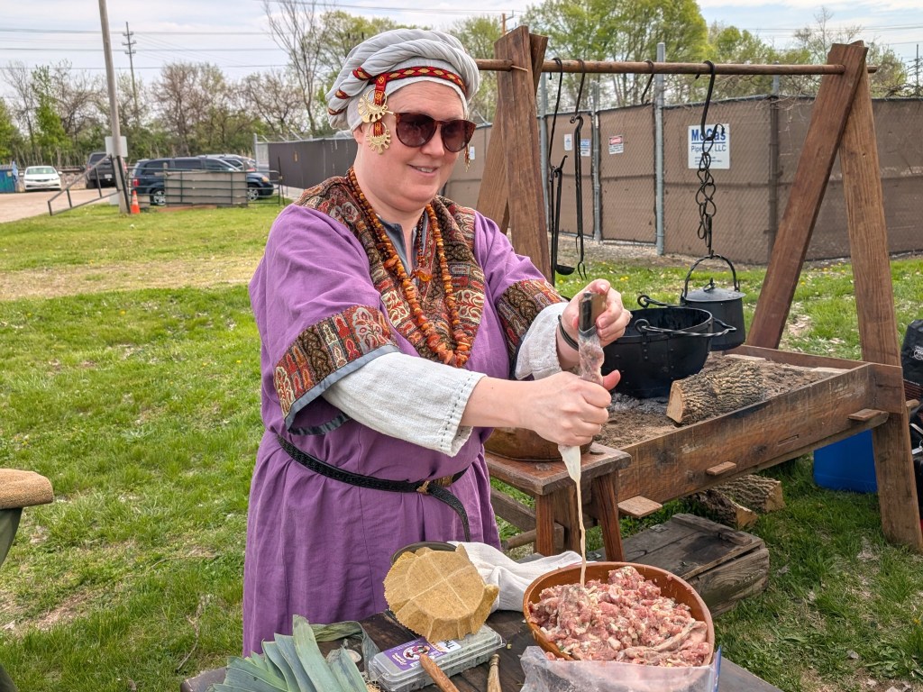 Random woman in medieval clothing, hand-stuffing sausage into a casing