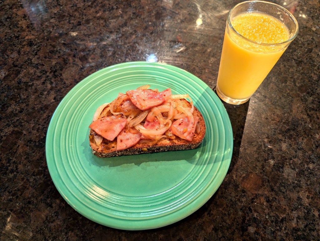 bacon and onions layered on a piece of toast with a glass of orange juice