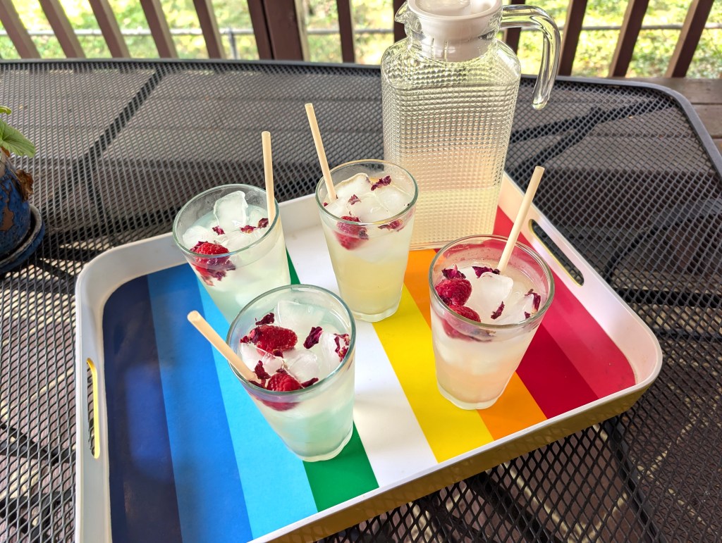 Rose lemonade in glasses of ice with straws, raspberries, and dried rose petals