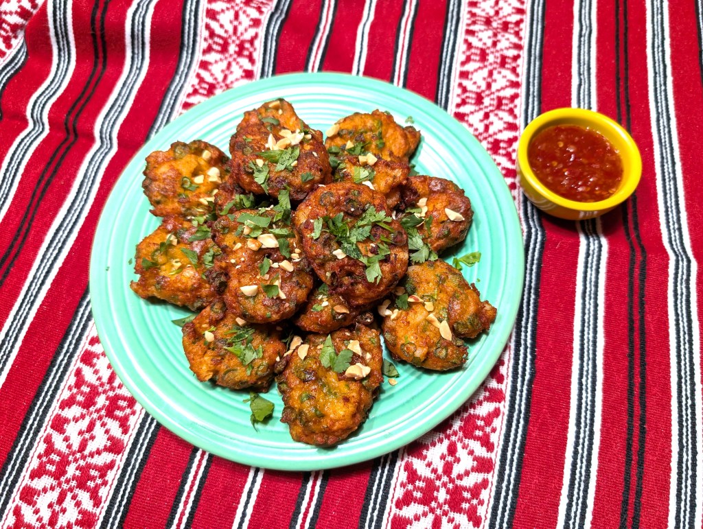 Seafood fritters on a plate with a small bowl of sweet chili sauce