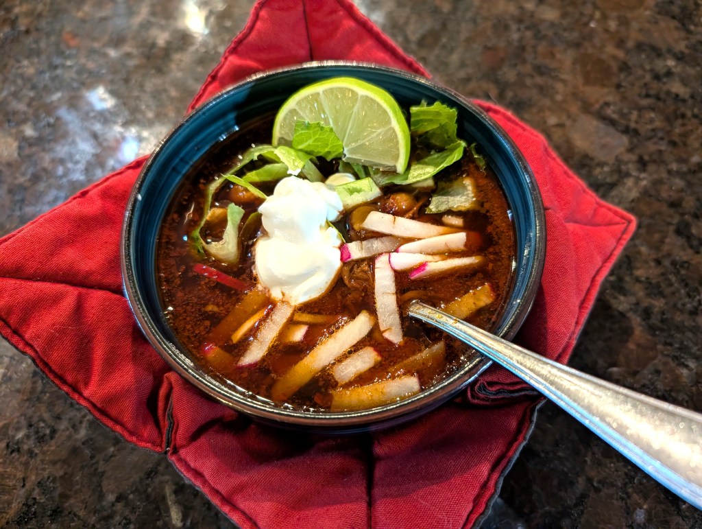 pozole with radish slices, lettuce, sour cream, and a lime wedge