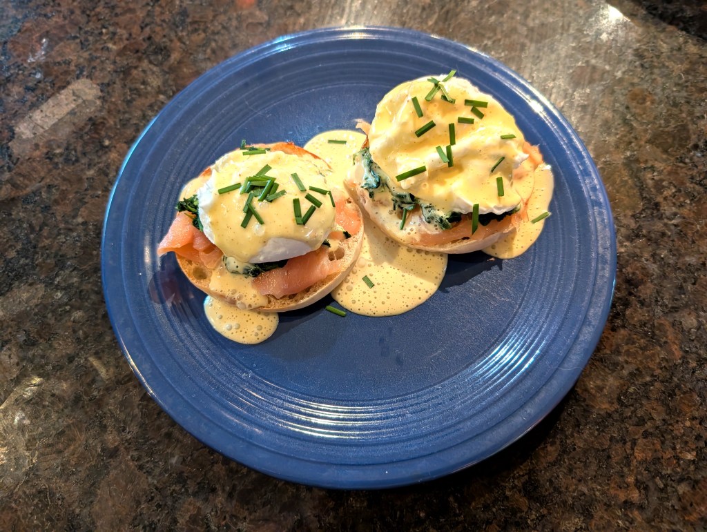 2 portions on a plate: 1 whole English muffin cut in half, with 2 poached eggs, smoked salmon, spinach, hollandaise sauce, and chives.